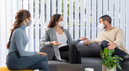 medium-shot-coworkers-couch-with-masks_23-2148862065